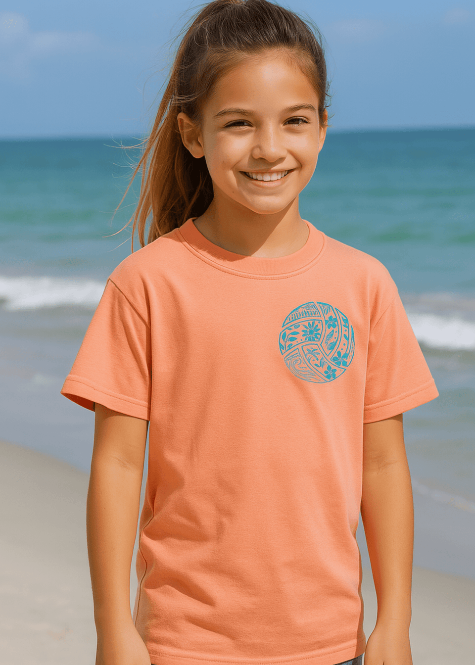 Young girl wearing a peach-colored t-shirt with a graphic design on a beach.